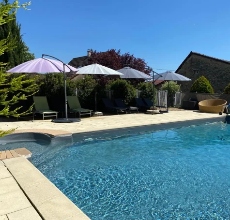 Vue d'ensemble de la piscine avec parasols mauves et maison en pierre Vue d'ensemble de la piscine avec parasols mauves et maison en pierre